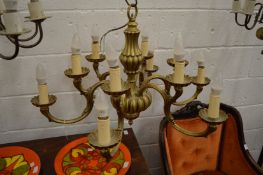 An ornate brass chandelier with six scrolling branches, each with two light fittings.
