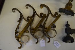 A set of three ornate brass curtain rail brackets.