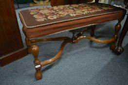 An upholstered long stool on turned legs with X shaped stretcher.