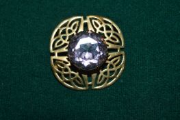 A decorative gilt metal brooch set with an amethyst coloured stone.
