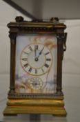 A brass carriage clock with alarm, porcelain panels to the face and sides, one side panel cracked.