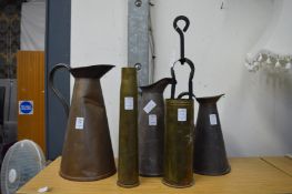 A graduated set of three copper jugs, two brass shell cases and a pair of coal tongs.
