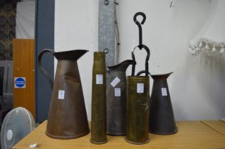 A graduated set of three copper jugs, two brass shell cases and a pair of coal tongs.