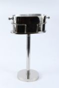 A POLISHED METAL OVAL SHAPE WINE BOTTLE HOLDER ON STAND. 64cms high.