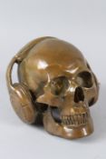 AN UNUSUAL BRONZE MODEL OF A SKULL WEARING HEADPHONES. 20cms wide.