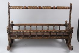 A 19TH CENTURY ISLAMIC HARDWOOD CRADLE, with mother-of-pearl inlay and turned decoration. 92cms long