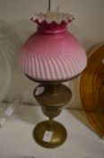 A brass lamp with opaque pink glass shade.