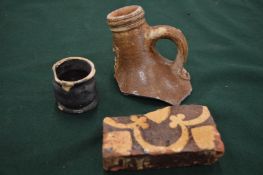 A fragment of Medieval tile together with a small Tudor pot and fragment of a Bellarmine jug.