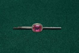 A bar brooch mounted with a pink stone.