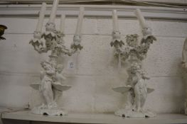 A pair of white porcelain candelabra with cherub and shell supports.