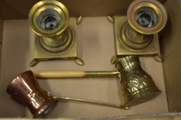 A pair of brass candlesticks and two metal pouring jugs.