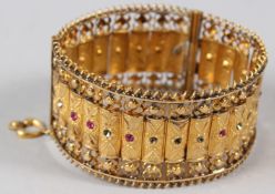 A MIDDLE EASTERN YELLOW METAL AND GEM SET FILIGREE STYLE BANGLE, with embossed and engraved panels