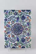 A LARGE OTTOMAN TURKISH IZNIK TILE, painted in blue, red and green with a stylised floral design.