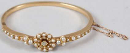 A YELLOW METAL, DIAMOND AND PEARL BANGLE, with a flowerhead mount, with a central diamond and pearls