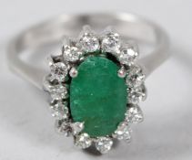A WHITE METAL, DIAMOND AND EMERALD CLUSTER RING.