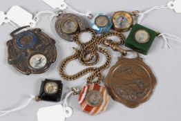 A COLLECTION OF SEVEN MINIATURE CHARM COMPASSES, and a motoring medallion.