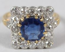 A YELLOW METAL, SAPPHIRE AND DIAMOND RING, the central sapphire within a square shaped diamond