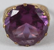 A 9CT GOLD DRESS RING, with ornate mount, set with an amethyst coloured stone.