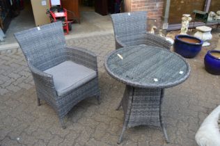 A modern wicker style patio set comprising pair of armchairs and glass topped table.