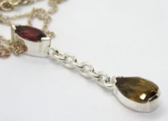 A silver pendant having pear cut stone suspended below red marquise cut stone,