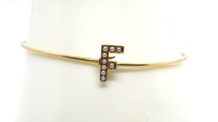 A 15ct gold bangle having seed pearl encrusted 'F' upon, engraved 1922-31, stamped 15ct, 5g.