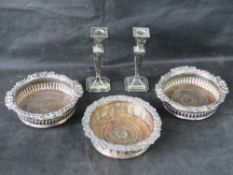 Three silver plated wine coasters together with a pair of silver plated candle sticks.