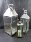 A set of three graduated glazed stainless steel lanterns.