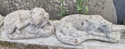 Two concrete garden figurines of recumbent dogs.