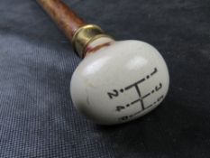 A walking stick featuring a cream-coloured ceramic knob modeled after a 5-speed manual gear shifter.