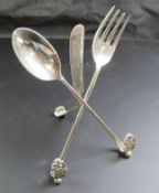 A silver plated menu holder in the form of an oversized knife, fork and spoon, 22cm high.