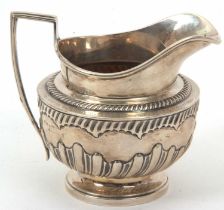 An early 19th Century silver cream jug of compressed circular form, having a gadrooned rim, part