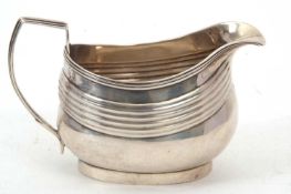 A George III silver cream/milk jug of compressed oval form, having a decorated reeded rim, handle,