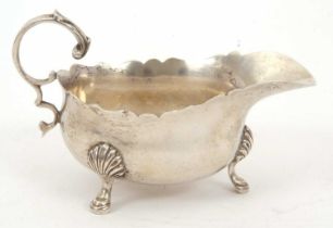 A George V silver sauce boat of typical form, having a wavey rim, a flying capped scrolled handle,