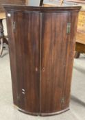 A George III mahogany bow front wall mounted corner cabinet fitted with two doors opening to a