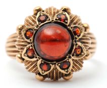 A garnet dress ring, with central round garnet cabochon, surrounded by gold petals set with small