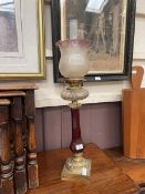 An ornate brass and glass oil lamp with cranberry glass column
