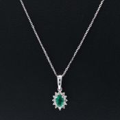 A 9CT WHITE GOLD EMERALD AND DIAMOND CLUSTER PENDANT NECKLACE.