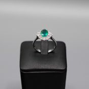 AN 18CT WHITE GOLD EMERALD AND DIAMOND CLUSTER RING.