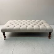 HEARTH STOOL IN BUTTONED NEUTRAL LINEN UPHOLSTERY ON TURNED SUPPORTS.