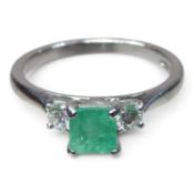 An 18 carat white gold emerald and diamond trilogy ring, the central square cut emerald, flanked