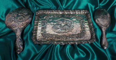 An Edwardian matched silver three piece dressing table set, repousse decorated with cherubs,