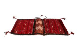 A Moroccan Berber kilim style wool carpet saddle bag. On a red ground with geometric patterns.