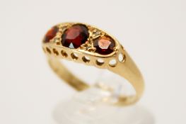 An 18ct gold and garnet three stone ring. In a pierced setting, the central stone circa 4.