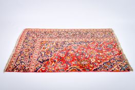 A 'cut down' Persian style woollen rug. Featuring a scrolling design on a red ground.
