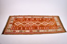 A Kilim rug runner. Having a geometric design in beige and pale blue on a red brown ground.
