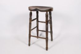 A 19th century elm barstool with saddle seat. Having turned supports united by stretchers.