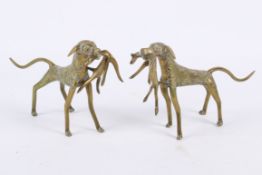 A pair of brass models of African dogs with prey.