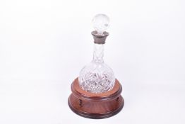 A silver collared claret jug on a wooden stand.