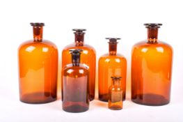 Six assorted apothecary or chemical amber glass storage bottles with stoppers.