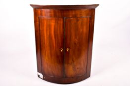 A George III mahogany veneered bow-front corner cupboard.
